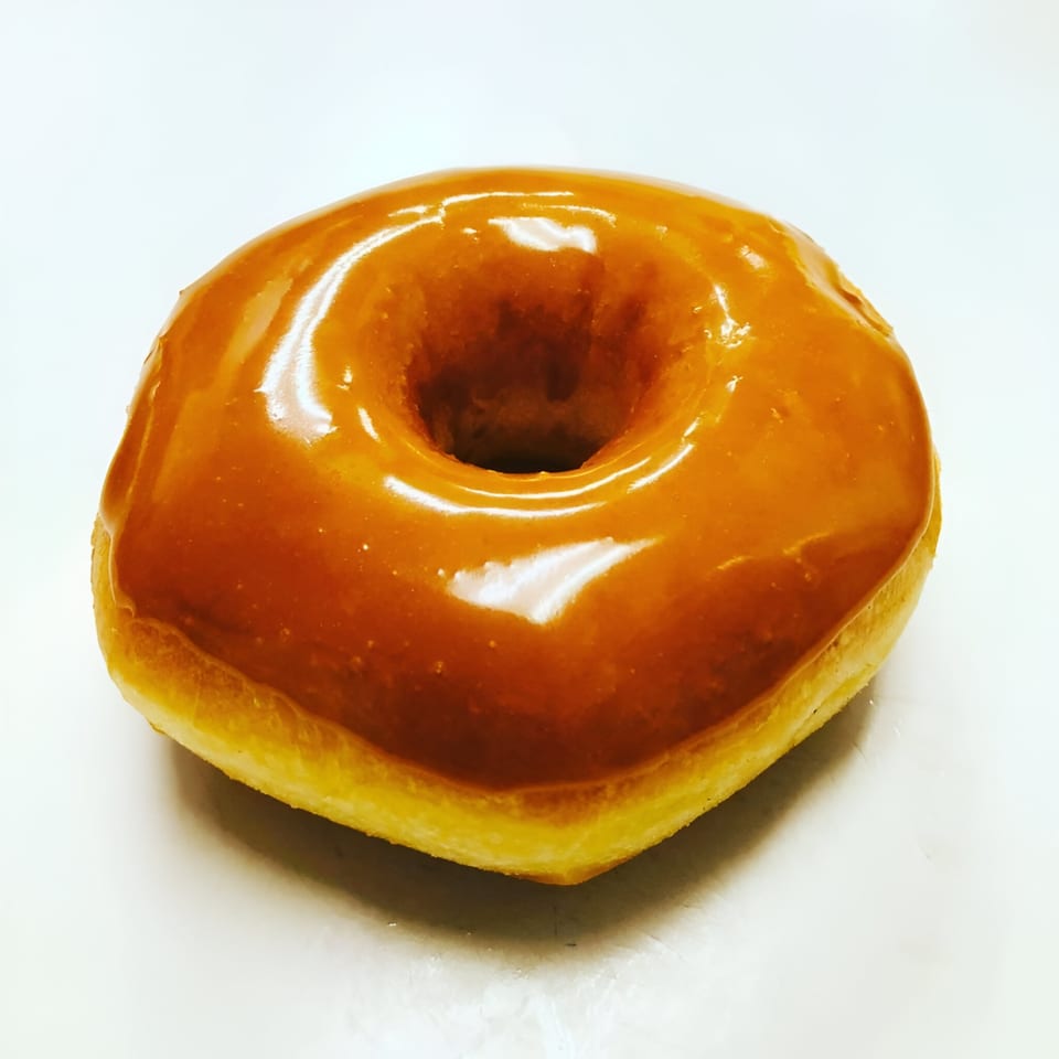 A single glazed donut from Donut Taco Palace, with a shiny caramel-colored topping.