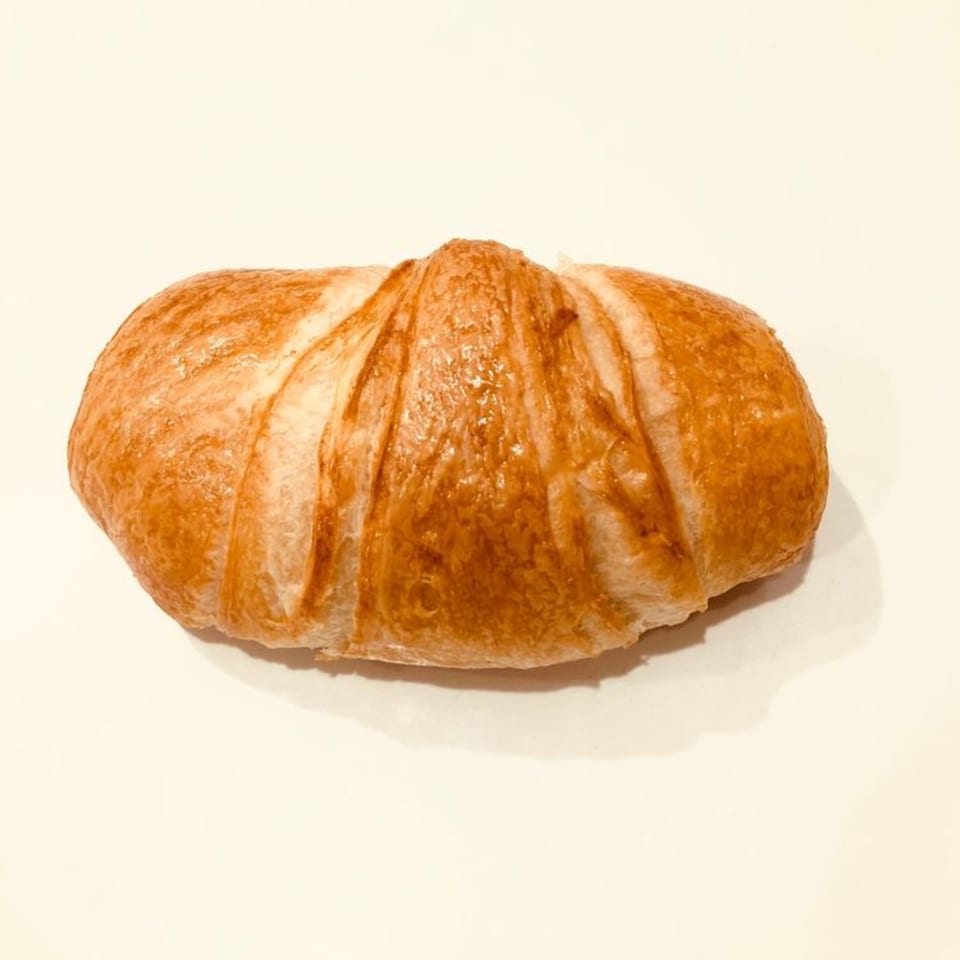 A golden-brown croissant, shiny and flaky, rests on a plain white surface.