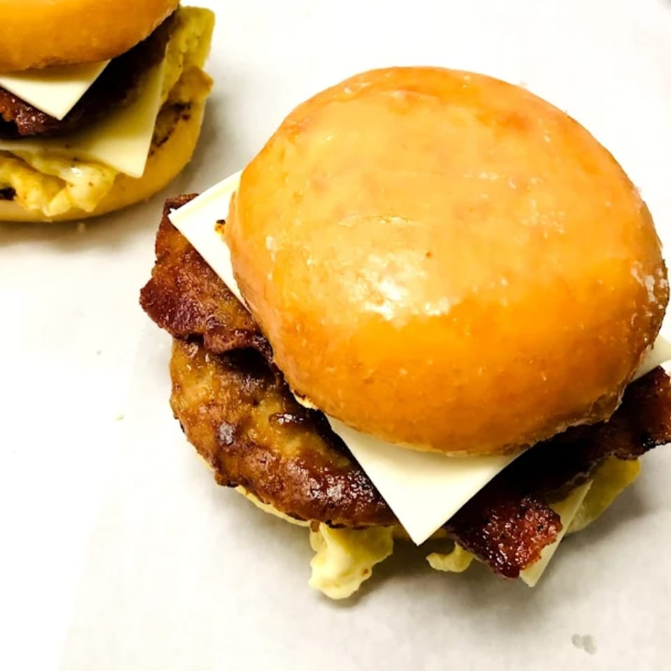 Two glazed donut breakfast sandwiches with bacon, egg, and cheese on a white surface.