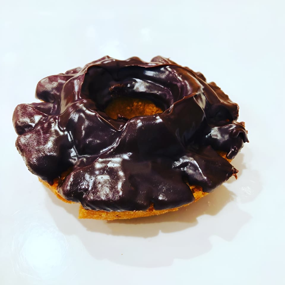 A chocolate-glazed old-fashioned donut from Donut Taco Palace on a white surface.