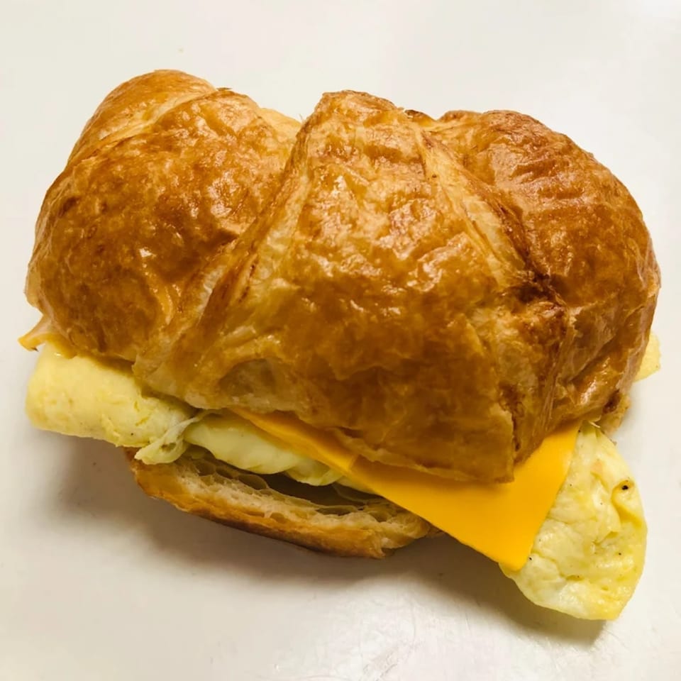 A golden-brown croissant breakfast sandwich with fluffy scrambled eggs and melted yellow cheese.