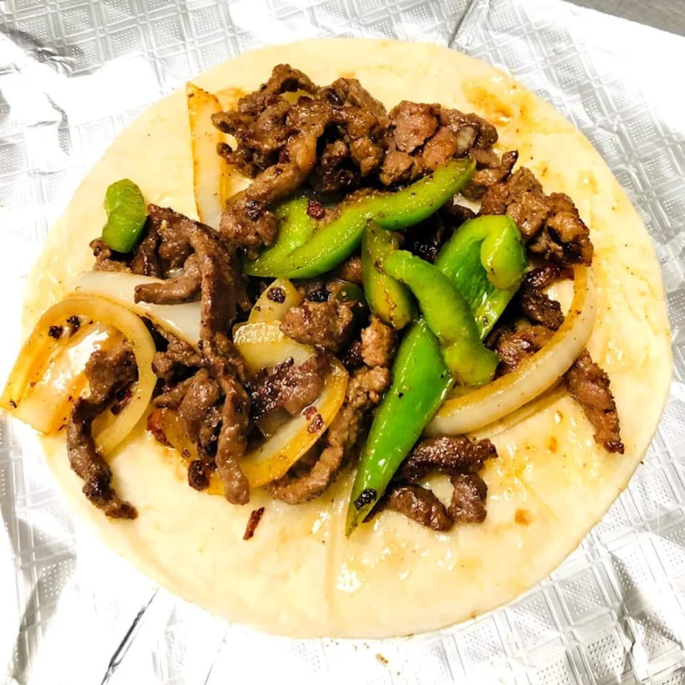A Donut Taco Palace taco filled with steak, grilled onions, and green bell peppers.