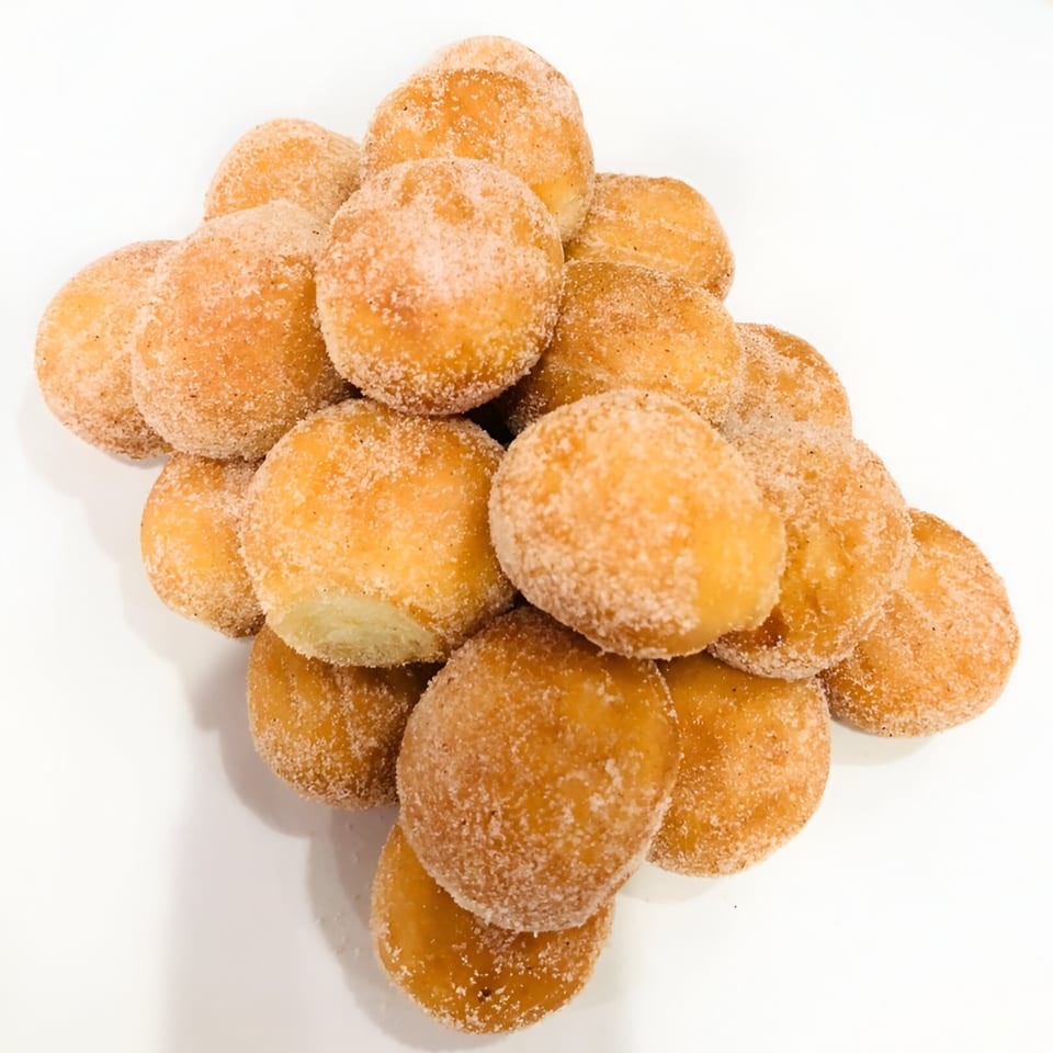 A pile of golden-brown donut holes, generously coated in cinnamon sugar, on a white surface.