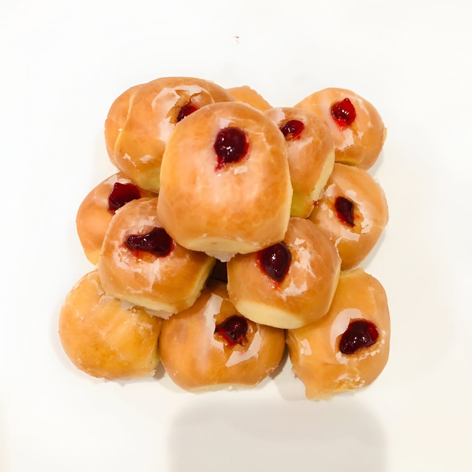 A pile of glazed Donut Taco Palace donuts filled with red jelly on a white background.